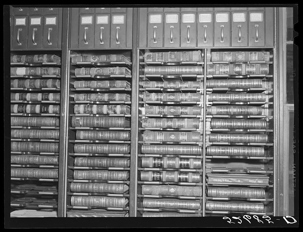 Black-and-white photograph of a county records vault, 1939. Steel shelving holds rows of leather-bound record books and deed indexes, each numbered and lettered on the spine; the words GRANVILLE COUNTY are legible on several. Labelled drawers run along the top.
